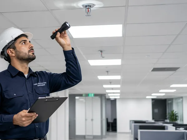 Fire protection engineer performing a routine sprinkler head inspection in a commercial office ceiling